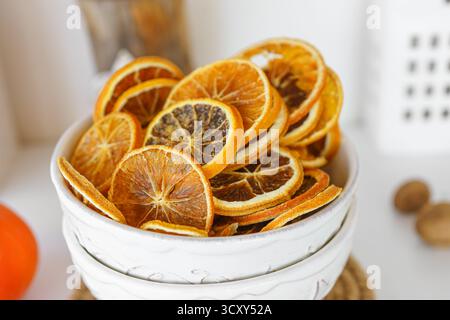 Les tranches d'orange séchées vibrantes sont méticuleusement empilées dans un bol blanc, mettant en valeur leurs couleurs et textures riches, tout en bénéficiant d'un fond de lumière naturelle douce. Banque D'Images