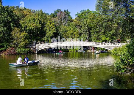 Le Bow Bridge à Central Park, Manhattan, New York City, avec des couples en barques dans le lac à la Ramble. Célèbre pont en fonte à New York. Banque D'Images