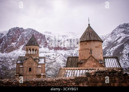 Une église qui est située dans les montagnes de l'Arménie. Les montagnes ont une teinte rougeâtre-orange et sont couvertes de neige. Banque D'Images