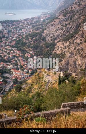 Baie de Kotor, Monténégro. Une vue imprenable sur une ville côtière nichée entre des montagnes imposantes, avec un grand bateau de croisière flottant dans la baie. Banque D'Images