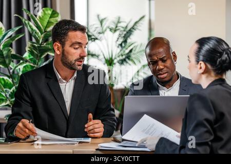 Groupe de professionnels des affaires collaborant à une réunion, analysant des documents et discutant des stratégies, entouré de plantes, mettant l'accent sur le travail d'équipe Banque D'Images