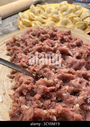 Boulettes maison non cuites sur la plaque dorée, viande hachée sur la plaque de bambou et un rouleau à pâtisserie sur la table noire dans la cuisine. Banque D'Images