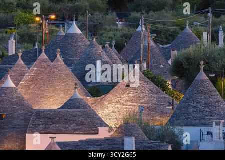 Une belle scène de soirée à Alberobello, dans les Pouilles, en Italie, avec les maisons traditionnelles trulli qui brillent doucement dans une lumière chaude. Les toits coniques et blancs Banque D'Images