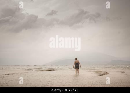 Une femme dans le vent marchant vers l'infini au-delà du bord de la mer Banque D'Images