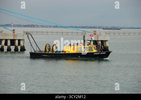 Un bateau Coast Diver jaune et noir près d'un quai dans les eaux côtières calmes, équipé de matériel de plongée et de drapeaux, utilisé pour les opérations sous-marines Banque D'Images