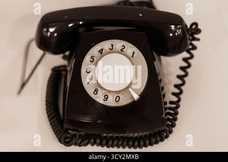 Un téléphone rotatif classique avec un cadran circulaire et un cordon enroulé repose sur une surface plane et lisse. L'extérieur noir ajoute une touche nostalgique, qui rappelle Banque D'Images