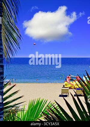 Lanzarote Puerto del Carmen plage palmiers et ciel bleu profond avec parachute de bateau et personnes swimmimg Banque D'Images