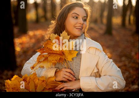 Mignonne femme souriante tenant des feuilles d'automne dans la nature Banque D'Images