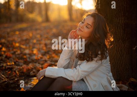 Jeune femme assise sous l'arbre et profitant de la journée ensoleillée d'automne Banque D'Images