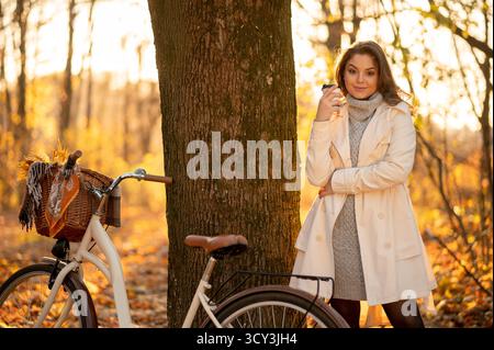 Femme se relaxant dans la forêt d'automne, tenant une tasse de café Banque D'Images
