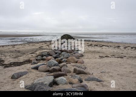 Un groyne en pierre fait de grands blocs de granit s'étend de la plage de sable sur l'île de Foehr loin dans les vasières, Schleswig-Holstein, Allemagne Banque D'Images