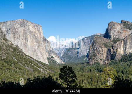 Les majestueux monolithes de granit, El Capitan et Half Dome, s'élèvent au-dessus des forêts denses de conifères de Yosemite Valley par une journée claire et ensoleillée. Banque D'Images