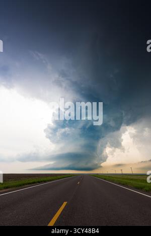 Un nuage d'orage impressionnant se profile au-dessus d'une route vide, capturant des cieux spectaculaires, l'isolement, la tension, les conditions météorologiques extrêmes, paysage ouvert, et la puissance brute Banque D'Images