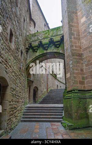 Mont Saint Michel, France – 15 décembre 2024 : une ruelle historique en pierre avec une arche et des marches, couverte de mousse verte vibrante, mettant en valeur l’anci Banque D'Images