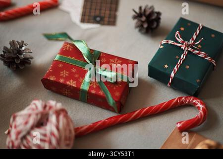 Cadeaux de Noël enveloppés dans du papier festif avec des rubans placés sur la table entouré de canne à bonbons, de pommes de pin et de ficelle, montrant en gros plan des cadeaux de vacances et des décorations saisonnières Banque D'Images