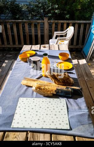 Vue d'une table de petit déjeuner avec jus d'orange, bols, assiettes et baguette au Camping Morbihan Plijadur à la Trinite sur mer dans le Morbihan en Bretagne Banque D'Images