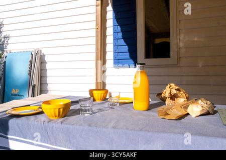 Vue d'une table de petit déjeuner avec jus d'orange, bols, assiettes et baguette au Camping Morbihan Plijadur à la Trinite sur mer dans le Morbihan en Bretagne Banque D'Images