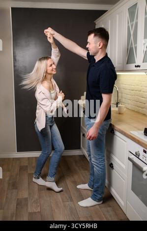 Couple in Love est à la date le jour de la Saint Valentin. Homme, femme dansent dans la cuisine, les femmes tourbillonnent, souriant joyeusement, se regardant amoureusement. Famille à emménager dans l'appartement loué, leur propre place Banque D'Images