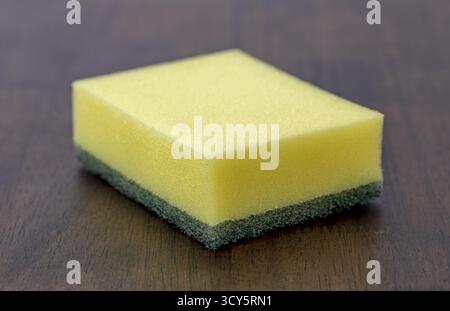 Une éponge jaune vert éponge de nettoyage éponge de cuisine éponge à vaisselle éponge de nettoyage ménager texture poreuse forme rectangulaire outil d'hygiène table en bois Banque D'Images