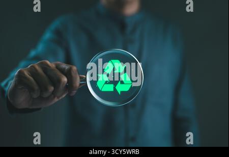 Planification du développement durable. Homme d'affaires tenant une loupe avec une icône de recyclage verte brillante, représentant le concept de durabilité Banque D'Images