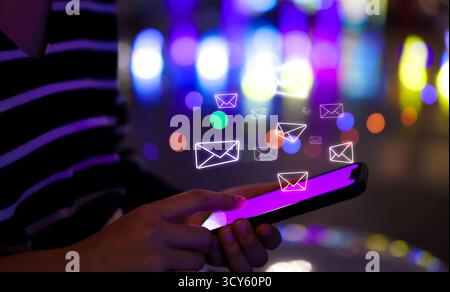 Concept d'alerte de notification par e-mail. Femme utilise un smartphone avec des icônes de messagerie brillantes au-dessus de l'écran, représentant la communication numérique et le courrier électronique Banque D'Images