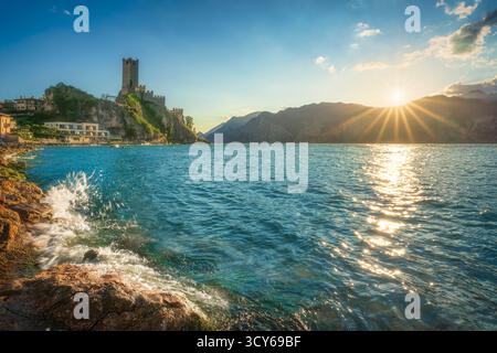 Spectaculaire coucher de soleil sur le château de Scaliger à Malcesine, lac de Garde. Sunburst sur les montagnes et lumière étincelante sur les vagues et les rochers dans la for Banque D'Images