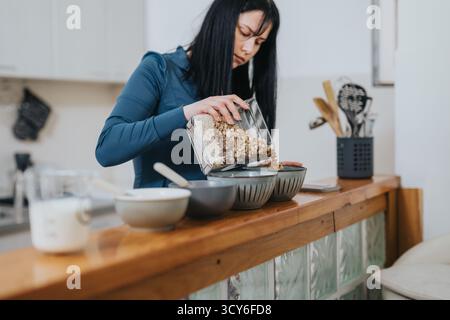 Jeune femme préparant un petit déjeuner de granola sain dans la cuisine Banque D'Images