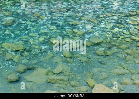 Une scène côtière tranquille avec une eau turquoise transparente et un lit de roches lisses et de galets. Idéal pour la nature, les voyages ou le style de vie côtier Banque D'Images