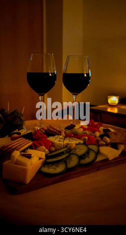 Soirée romantique aux chandelles avec deux verres de vin rouge et fromage gastronomique et planche à collations sur une table en bois. Banque D'Images