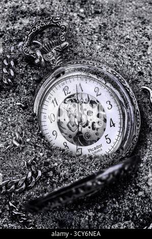 Bacau, Roumanie, 1er juillet 2015 : image en noir et blanc d'une montre de poche squelette avec des chiffres arabes, partiellement enterrée dans le sable. Banque D'Images
