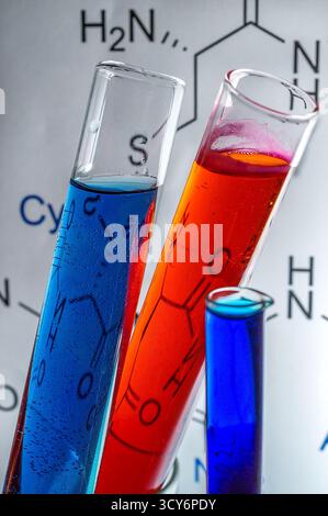 Trois tubes à essai remplis de liquides bleus, rouges et bleus foncés se dressent sur un fond de structures chimiques. Banque D'Images