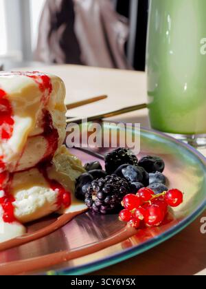 Gros plan de crêpes de soufflé moelleuses avec des baies et une garniture crémeuse à côté du latte matcha Banque D'Images