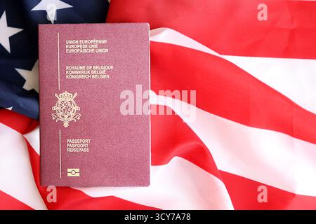 Passeport belge sur grand drapeau agitant des États-Unis d'Amérique close up. Visa AMÉRICAIN et concept d'immigration Banque D'Images
