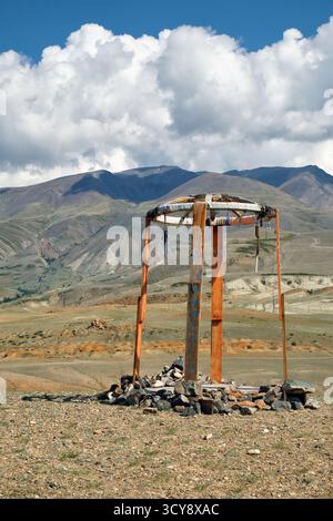 Construction religieuse en bois dans les montagnes de l'Altaï. Fait de poteaux et de pierres en bois. En arrière-plan chaîne de montagnes Kurai sous ciel bleu et nuages. Banque D'Images