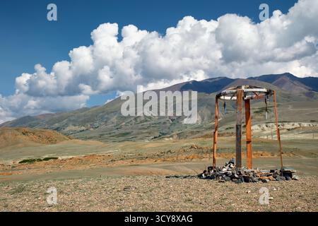 Construction religieuse en bois dans les montagnes de l'Altaï. Fait de poteaux et de pierres en bois. En arrière-plan chaîne de montagnes Kurai sous ciel bleu et nuages. Banque D'Images