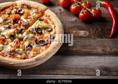 Pizza végétarienne avec champignons et olives sur une vieille table en bois et tomates fraîches, oignon vert et piment sur fond Banque D'Images