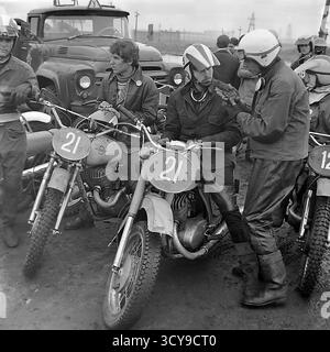 Une photo d'archives dynamique des années 1970 capture l'atmosphère gracieuse d'une course de motocross à Sloviansk, en RSS d'Ukraine. Les coureurs vêtus de casques vintage et d'équipements de protection chevauchent leurs puissantes motos de l'ère soviétique (probablement des modèles CZ ou Izh) sur une piste boueuse de terre, prêts pour la compétition. Les spectateurs se rassemblent à proximité, ajoutant à l'excitation de l'événement de sport automobile local. Cette image dépeint de manière éclatante la passion pour le sport et les rassemblements communautaires dans un Donbass pacifique avant la guerre Banque D'Images