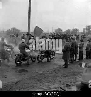 Une photo d'archives dynamique des années 1970 capture l'atmosphère gracieuse d'une course de motocross à Sloviansk, en RSS d'Ukraine. Les coureurs vêtus de casques vintage et d'équipements de protection chevauchent leurs puissantes motos de l'ère soviétique (probablement des modèles CZ ou Izh) sur une piste boueuse de terre, prêts pour la compétition. Les spectateurs se rassemblent à proximité, ajoutant à l'excitation de l'événement de sport automobile local. Cette image dépeint de manière éclatante la passion pour le sport et les rassemblements communautaires dans un Donbass pacifique avant la guerre Banque D'Images