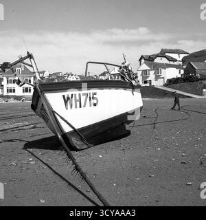 Image de film noir et blanc du bateau amarré sur la plage à marée basse avec l'homme marchant sur la plage et les maisons en arrière-plan Banque D'Images