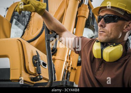 Un travailleur de la construction portant un casque de sécurité et des lunettes de sécurité fait fonctionner des machines tout en se concentrant sur la tâche sur un chantier de construction. Banque D'Images