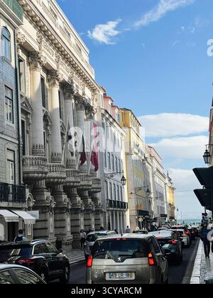 Lisbonne, Portugal - 28 septembre 2025 : scène de rue animée de Lisbonne avec de grands drapeaux de colonnes et des voitures le long d'une route ensoleillée de front de mer au Portugal. Banque D'Images