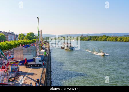 Mayence, Allemagne - 19 juin 2025 : scène fluviale dynamique à Mayence avec une atmosphère festive avec des manèges, un bateau naviguant sur le Rhin, et l Banque D'Images