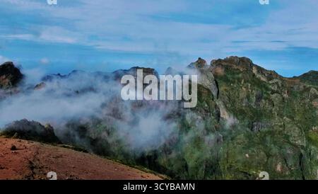 Paysage montagneux brumeux avec des falaises spectaculaires, lumière du matin et rochers rougeâtres. Les nuages éthérés dérivent à travers des vallées vertes. Parfait pour la nature, trav Banque D'Images
