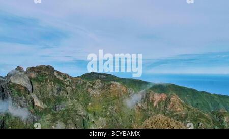 Paysage montagneux brumeux avec des falaises spectaculaires, lumière du matin et rochers rougeâtres. Les nuages éthérés dérivent à travers des vallées vertes. Parfait pour la nature, trav Banque D'Images