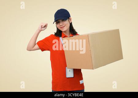 livraison jeune travailleur en uniforme rouge tenant une grande boîte en carton avec une expression fière et confiante Banque D'Images