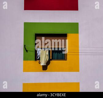 Vêtements suspendus à une fenêtre sur une façade colorée de bâtiment. Banque D'Images