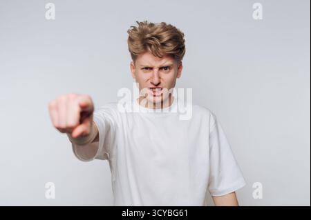 Un jeune homme aux cheveux blonds touffus affiche une colère et une frustration visibles. Il pointe vers l'avant, comme s'il faisait une déclaration ou un argument fort, encore une fois Banque D'Images