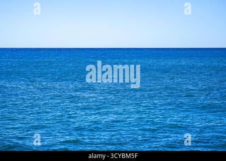 Une vue imprenable sur l'eau calme de l'océan bleu sous un ciel bleu clair avec des vagues douces lançant à la surface, reflétant le soleil et la sérénité Banque D'Images