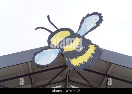 Grand logo bourdon monté au-dessus du toit d'entrée du Haskins Garden Centre, symbolisant la nature, le jardinage et une atmosphère de vente au détail conviviale. Banque D'Images