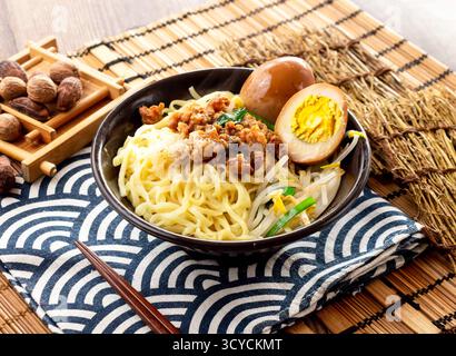 Nouilles de pâtes sèches chinoises avec viande de porc hachée, œuf en conserve et baguettes servies dans un plat isolé sur la serviette vue de côté sur la table nourriture taïwanaise Banque D'Images